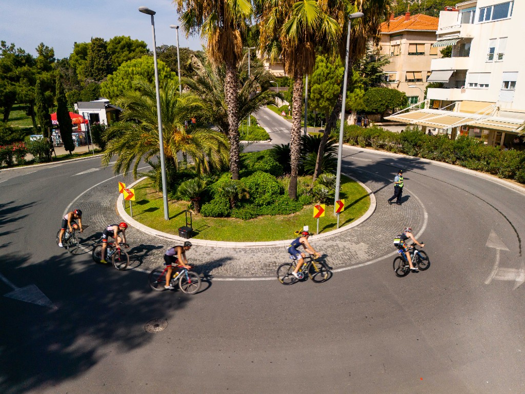 Cyclists racing through a palm-lined roundabout on race day